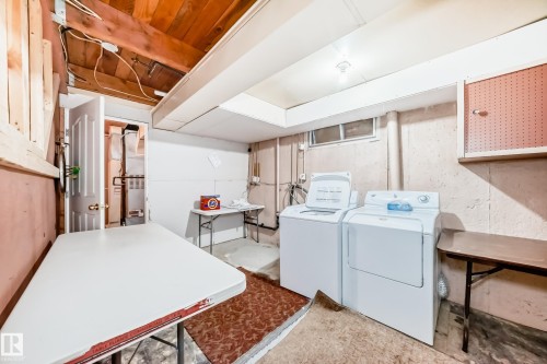 Equipped laundry area featuring a freestanding washer and dryer, exposed wood ceiling beams, a utility sink, and a high-set window - 6804 102A Avenue, Edmonton, AB 