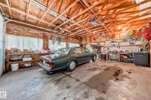 Spacious garage featuring an exposed wood truss ceiling, concrete flooring, and extensive built-in shelving - 6804 102A Avenue, Edmonton, AB 