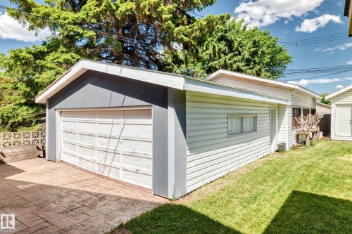 Detached garage featuring a white panel door, light gray stucco facade, white siding, and stamped concrete paving - 6804 102A Avenue, Edmonton, AB 
