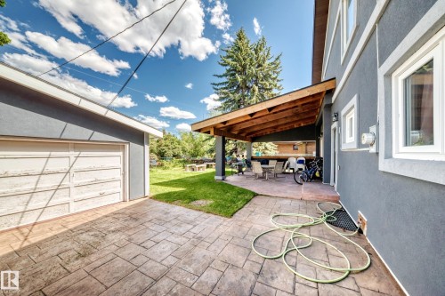 Stamped concrete patio with a covered outdoor living area featuring exposed wood beams, a stucco exterior, and a detached garage with an overhead door - 6804 102A Avenue, Edmonton, AB 