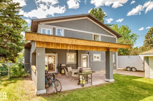 Rear exterior featuring a covered patio with concrete flooring, stucco siding, a sliding glass door, and a grass lawn - 6804 102A Avenue, Edmonton, AB 