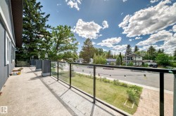 Concrete balcony with a glass and metal railing, featuring a stucco exterior, multiple exterior light fixtures, and a tree-lined streetscape - 