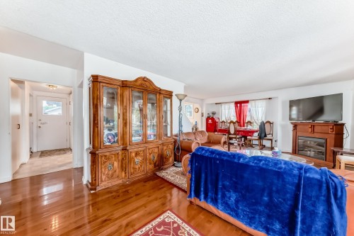 Open-concept living space featuring wood-finish flooring, a decorative fireplace with a wood-finish mantel, and a bright entryway with a frosted glass door - 6804 102A Avenue, Edmonton, AB 