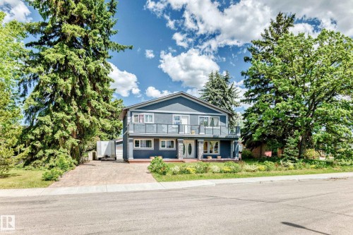 Two-story residence featuring a balcony with glass railings, stone-accented pillars, a multi-pane front door, and a paved driveway - 6804 102A Avenue, Edmonton, AB 