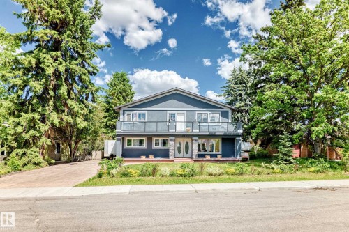 Two-story residence featuring a balcony with glass railing, a stone facade accent, and mature trees - 6804 102A Avenue, Edmonton, AB 