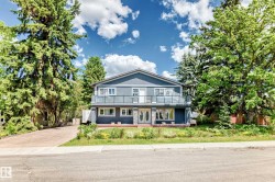 Two-story residence featuring a balcony with glass railing, a stone facade accent, and mature trees - 