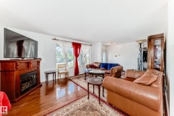 Warm and inviting living area featuring wood-finish flooring, a decorative electric fireplace with a wood-tone mantel, and a large window providing ample natural light - 