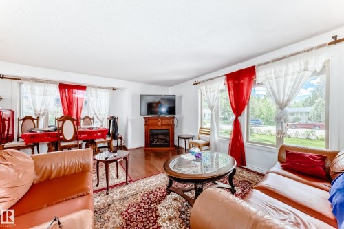 Hardwood-finish flooring extending into the dining area, large picture windows, wood-finish fireplace mantel with an electric insert, and white textured ceilings - 6804 102A Avenue, Edmonton, AB 
