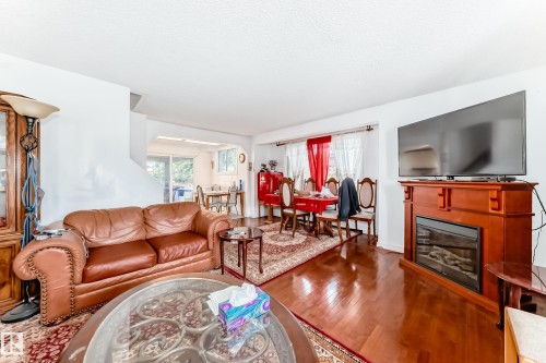 Living area featuring glossy wood-finish flooring, a built-in fireplace with a wood-tone mantel, and a recessed archway - 6804 102A Avenue, Edmonton, AB 