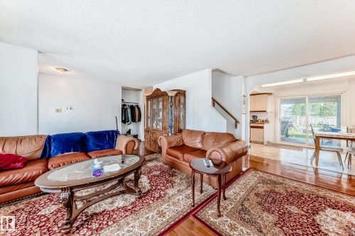 Living area featuring wood-finish flooring, a staircase with a wooden handrail, and an open doorway leading to a dining area with sliding glass doors - 6804 102A Avenue, Edmonton, AB 