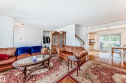 Living area featuring wood-finish flooring, a staircase with a wooden handrail, and an open doorway leading to a dining area with sliding glass doors - 