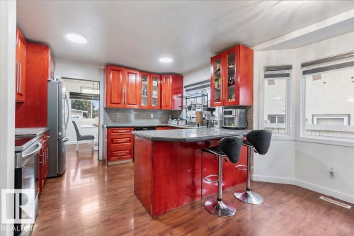 Kitchen featuring red wood cabinetry, stainless steel appliances, a center island with bar seating, a bay window, and wood-finish flooring - 712 Lee Ridge Road, Edmonton, AB 