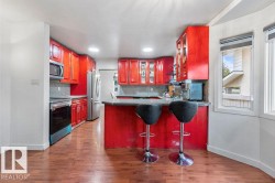 Kitchen featuring red cabinetry, wood-finish flooring, stainless steel appliances, a bar-height countertop, and multiple windows with blinds - 