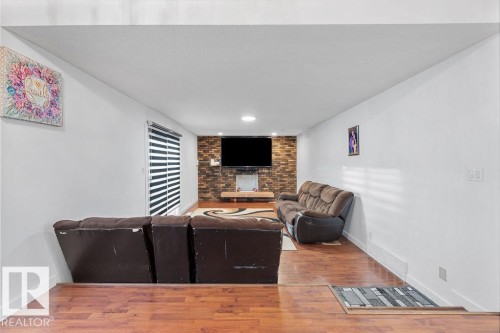 Spacious room featuring wood-finish flooring, white painted walls, and a brick accent wall with a mounted fixture - 712 Lee Ridge Road, Edmonton, AB 