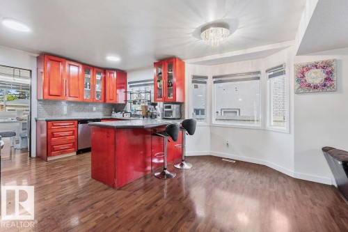 Kitchen featuring red cabinetry, stainless steel appliances, a breakfast bar island, and wood-finish flooring - 712 Lee Ridge Road, Edmonton, AB 