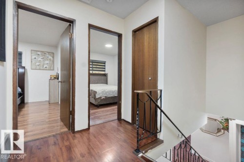 Upper-level landing featuring wood-finish flooring, white walls, and a staircase with an ornamental metal railing - 712 Lee Ridge Road, Edmonton, AB 