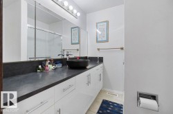 Bathroom vanity featuring a vessel sink, dark countertop, and white cabinetry with brushed nickel hardware - 