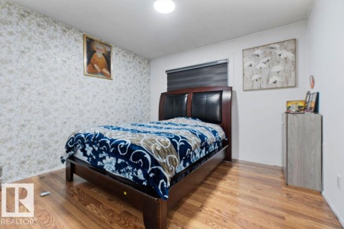 Bedroom featuring a textured accent wall, wood-finish flooring, a contemporary ceiling light fixture, and a window with blinds - 712 Lee Ridge Road, Edmonton, AB 