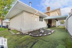 Rear exterior featuring textured stucco siding, an attached awning, a brick chimney, white fencing, and a section of artificial turf - 