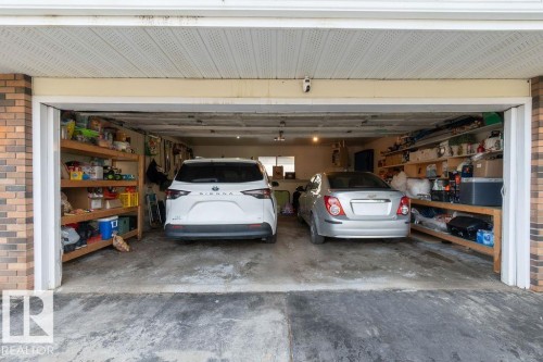 Attached two-car garage with a concrete floor, featuring built-in wooden shelving for organization - 712 Lee Ridge Road, Edmonton, AB 