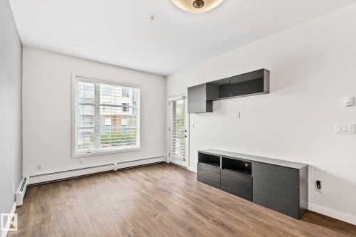 Spacious room featuring wood-finish flooring, white walls, and a large window with horizontal blinds - 217 2588 Anderson Way, Edmonton, AB 