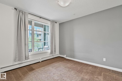 Room featuring a large window with white framing, neutral carpeting, and baseboard heating - 217 2588 Anderson Way, Edmonton, AB 
