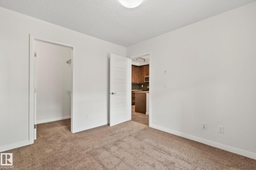 Neutral-toned carpeted room featuring a ceiling-mounted light fixture, white walls, and white trim - 217 2588 Anderson Way, Edmonton, AB 