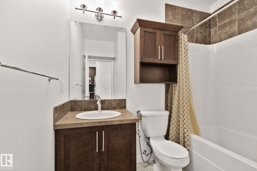Bathroom featuring a wood-finish vanity with an integrated sink, a rectangular mirror, and overhead vanity lighting - 217 2588 Anderson Way, Edmonton, AB 