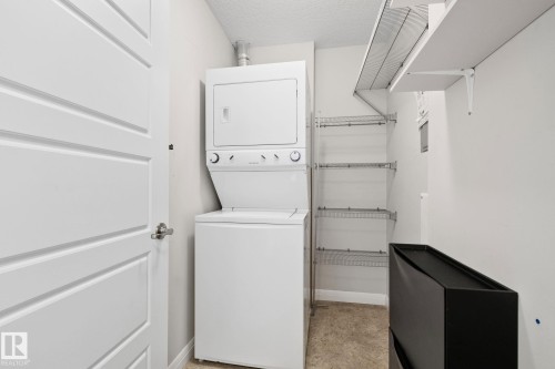 Dedicated laundry area featuring a stacked washer and dryer, adjacent to a wall of wire shelving for storage - 217 2588 Anderson Way, Edmonton, AB 