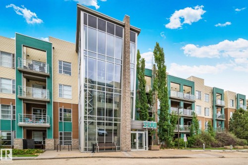 Modern multi-story building featuring a prominent glass-enclosed entrance, stacked stone accents, and varied siding in shades of beige and teal - 217 2588 Anderson Way, Edmonton, AB 