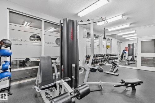 Fitness center featuring a comprehensive selection of exercise equipment, rubber flooring, and large mirrored walls - 217 2588 Anderson Way, Edmonton, AB 