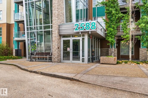 Modern building entrance featuring contemporary glass doors, a stone facade, and prominent building numbering - 217 2588 Anderson Way, Edmonton, AB 