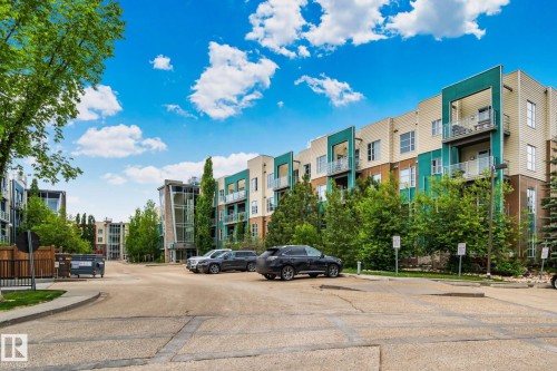 Modern multi-story building featuring balconies with metal railings, a teal and tan facade, and extensive surrounding landscaping - 217 2588 Anderson Way, Edmonton, AB 