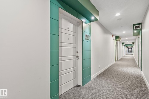 Hallway featuring patterned carpeting, recessed lighting, white walls, and teal accents surrounding entry doors - 217 2588 Anderson Way, Edmonton, AB 