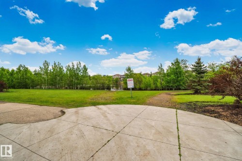 Expansive green space featuring a concrete patio, mature trees, and a distant body of water - 217 2588 Anderson Way, Edmonton, AB 