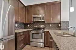 Kitchen featuring stainless steel appliances, dark wood cabinetry, a subway tile backsplash, and speckled countertops - 