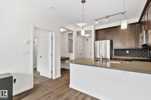 Kitchen island featuring a light-toned stone countertop, integrated sink, and modern pendant lighting - 217 2588 Anderson Way, Edmonton, AB 