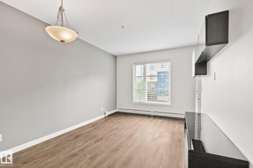 Spacious room featuring wood-finish flooring, a large window with blinds, and a contemporary ceiling fixture - 217 2588 Anderson Way, Edmonton, AB 