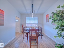 Dining area featuring wood-finish flooring, a contemporary linear chandelier, and a large window with privacy blinds - 