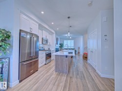 Contemporary kitchen featuring stainless steel appliances, white cabinetry, a wood-finish island with a white countertop, and recessed lighting - 