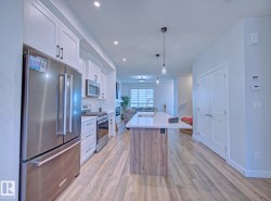 Modern kitchen featuring white cabinetry, stainless steel appliances, a center island with pendant lighting, and wood-finish flooring - 
