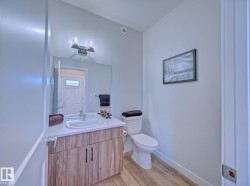 Bathroom featuring a wood-finish vanity with a white countertop and integrated sink, above-vanity lighting, wall-mounted mirror, and wood-finish flooring - 