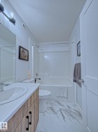 Bathroom featuring a full vanity with wood-finish cabinetry and a white countertop, a built-in tub and shower combination with a shower rod, and white marble-look floor tiles - 