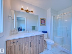 Contemporary bathroom featuring a wood-finish vanity with a white countertop and undermount sink, a large mirror, a three-bulb vanity light fixture, a walk-in shower with a glass enclosure, and white tiled flooring - 