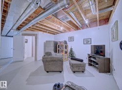 Finished basement space featuring exposed ceiling joists and ductwork, white walls, light gray flooring, and recessed lighting - 