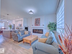 Open-concept living space featuring wood-finish flooring, a contemporary fireplace with a white mantel, and a kitchen island with pendant lighting - 