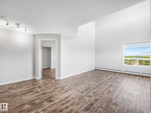 Spacious room featuring wood-finish flooring, white walls, and a large window with horizontal blinds - 2406 320 Clareview Station Drive, Edmonton, AB 