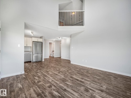 Spacious open-concept living area featuring wood-finish flooring, vaulted ceilings, and a kitchen with stainless steel appliances - 2406 320 Clareview Station Drive, Edmonton, AB 