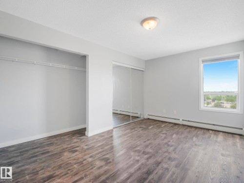 Spacious room featuring wood-finish flooring, a generous window, and a full-wall mirrored closet - 2406 320 Clareview Station Drive, Edmonton, AB 