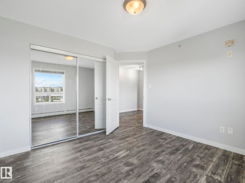 Bedroom featuring mirrored closet doors, wood-finish flooring, and white trim - 2406 320 Clareview Station Drive, Edmonton, AB 